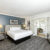 Modern hotel room with a large bed, two lamps, and open French doors leading to a bright sitting area.