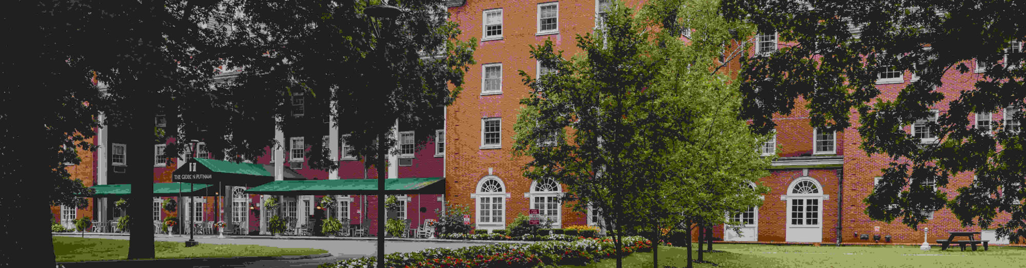 Red-brick building with arched windows, surrounded by trees, green lawn, and colorful flowerbeds.