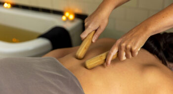 Person receiving a bamboo massage on their back in a spa setting with lit candles in the background.