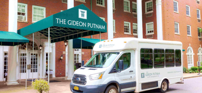 A white shuttle bus parked in front of The Gideon Putnam hotel entrance with green awning.