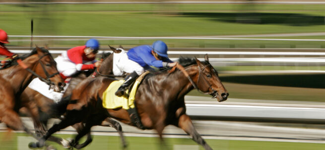 Three jockeys race horses at high speed on a racetrack, blurred background shows motion.