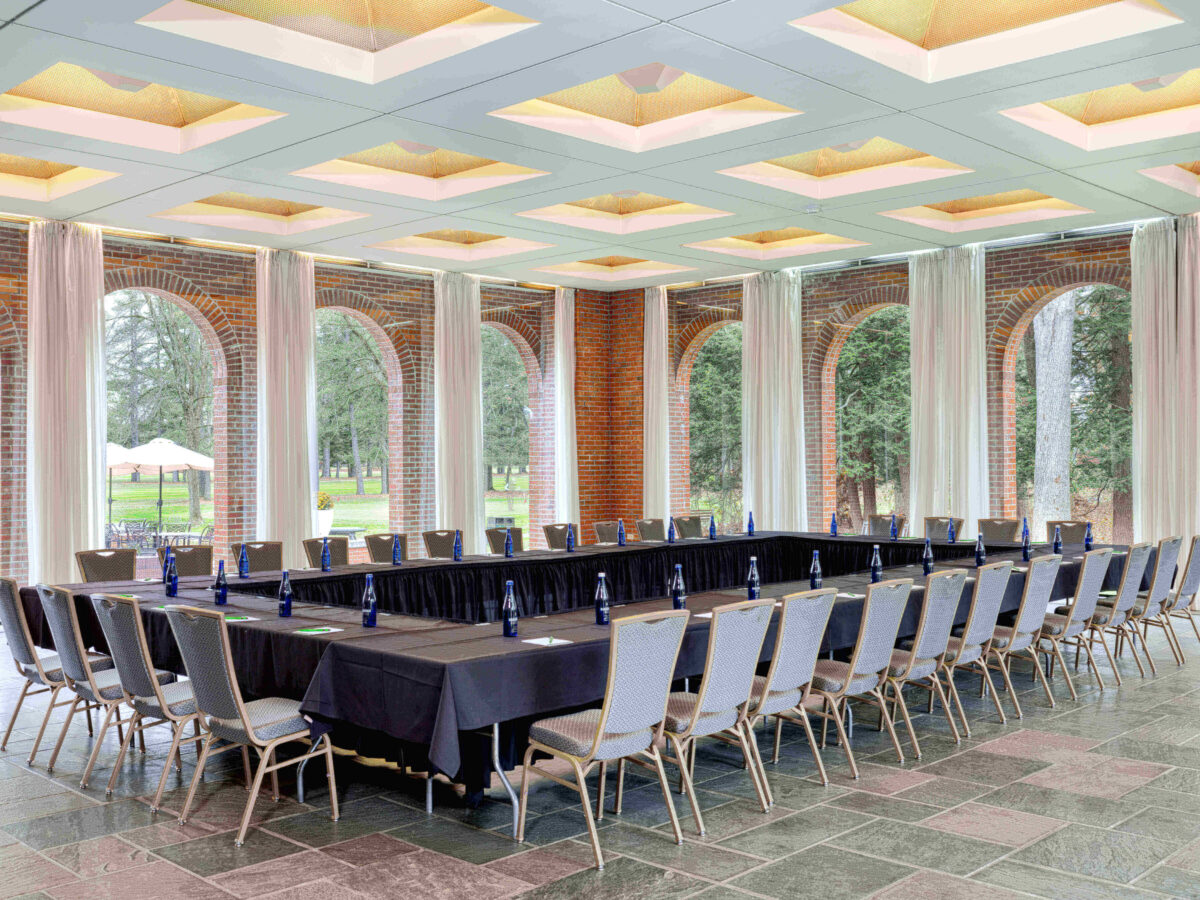 Conference room with U-shaped table setup, chairs, water bottles, and large windows overlooking greenery.