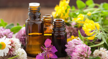 Three small amber glass bottles surrounded by colorful wildflowers on a wooden surface.