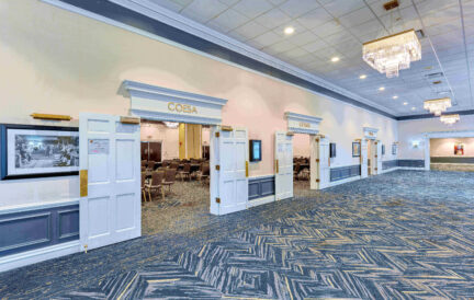 Spacious hallway with open doors to meeting rooms, chandeliers, and patterned carpet in a convention center.