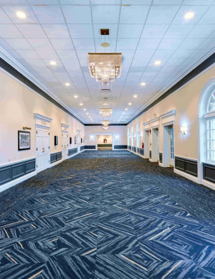 A hallway with blue carpet and chandeliers.