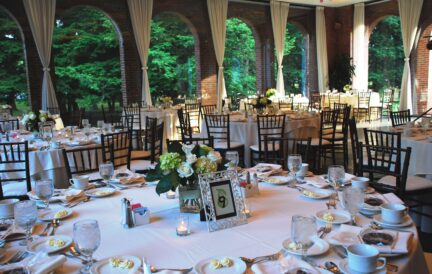 Elegant banquet hall with round tables, white tablecloths, floral centerpieces, and large windows.
