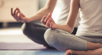 Two people sitting cross-legged on yoga mats, meditating with hands in a mudra position.